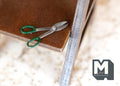 1:12 scale miniature tin shears with green handles and silver blades, shown on a workbench beside a ruler