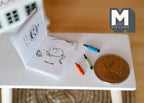 1:12 scale miniature coloring book with 3 crayons in blue, green and orange, shown open beside a coin for scale