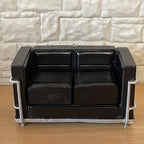 1:12 scale miniature cast resin modern loveseat in black with silver frame and solid cushions, by a white stone wall