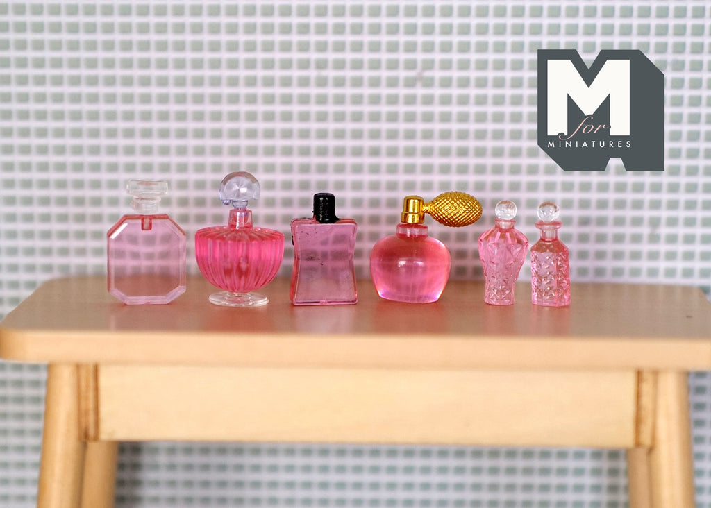1:12 scale miniature perfume and toiletry bottles in pink, set of 6, assorted shapes shown in a row on a wood table
