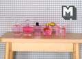 1:12 scale miniature perfume and toiletry bottles in pink, set of 6, assorted shapes shown in a row on a wood table