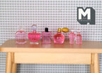 1:12 scale miniature perfume and toiletry bottles in pink, set of 6, assorted shapes shown in a row on a wood table