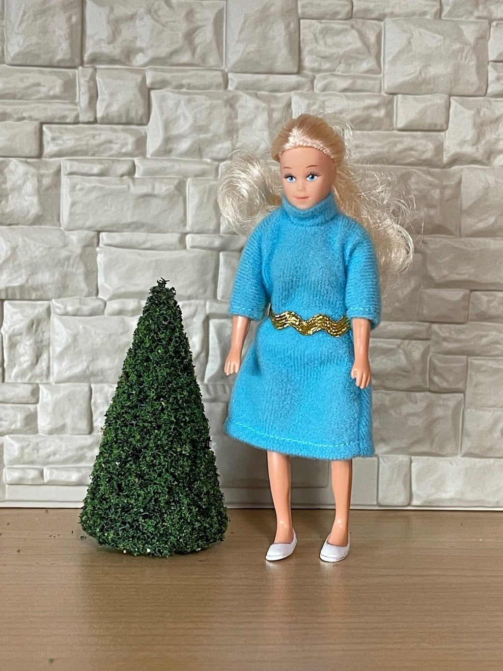 1:12 scale miniature foam evergreen tree in a dark green cone shape, shown beside a figure in a blue dress