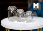 1:12 scale miniature clear glass round canisters with lids and wire clasps, set of 3, shown on a round white table