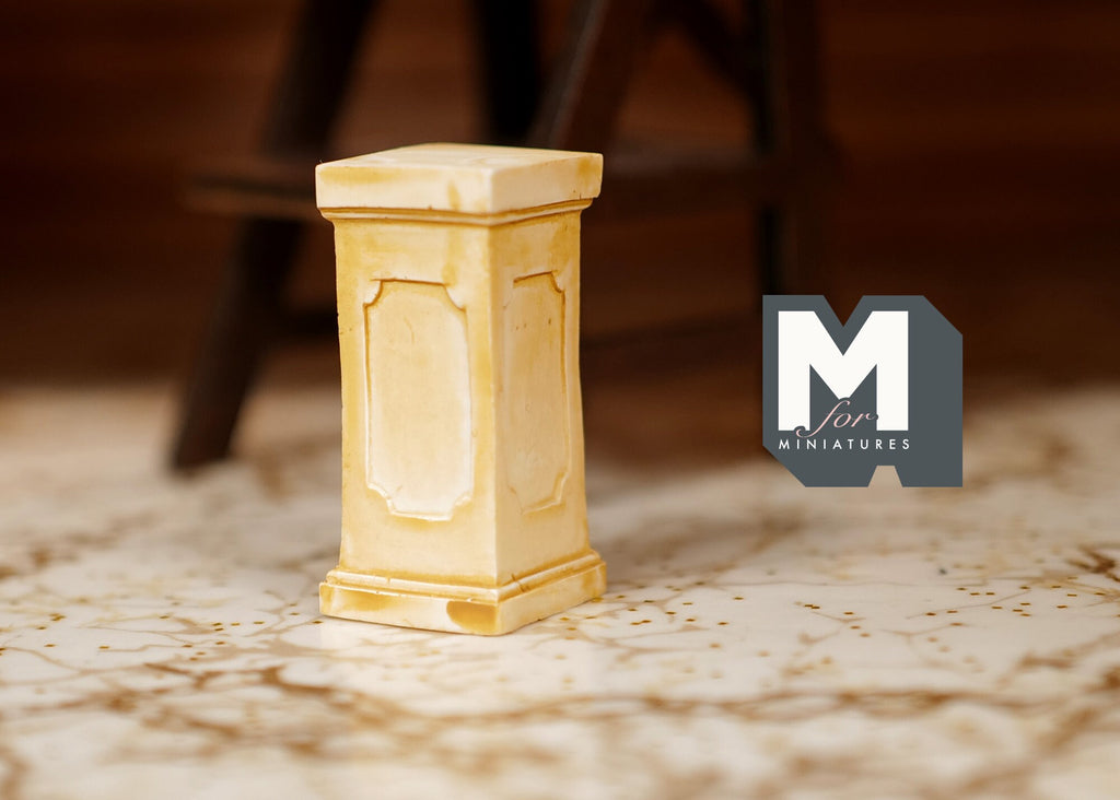 1:12 scale miniature square plant pedestal in beige with panel detail, shown on a patterned rug