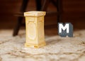 1:12 scale miniature square plant pedestal in beige with panel detail, shown on a patterned rug