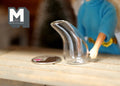 1:12 scale miniature clear glass wine decanter in a swan shape, shown on a table beside a coin and a doll hand