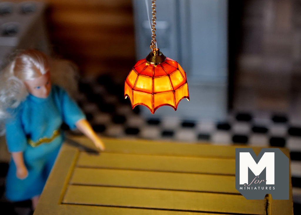 1:12 scale miniature stained glass style pendant light in red and orange, battery powered, shown lit above a yellow table