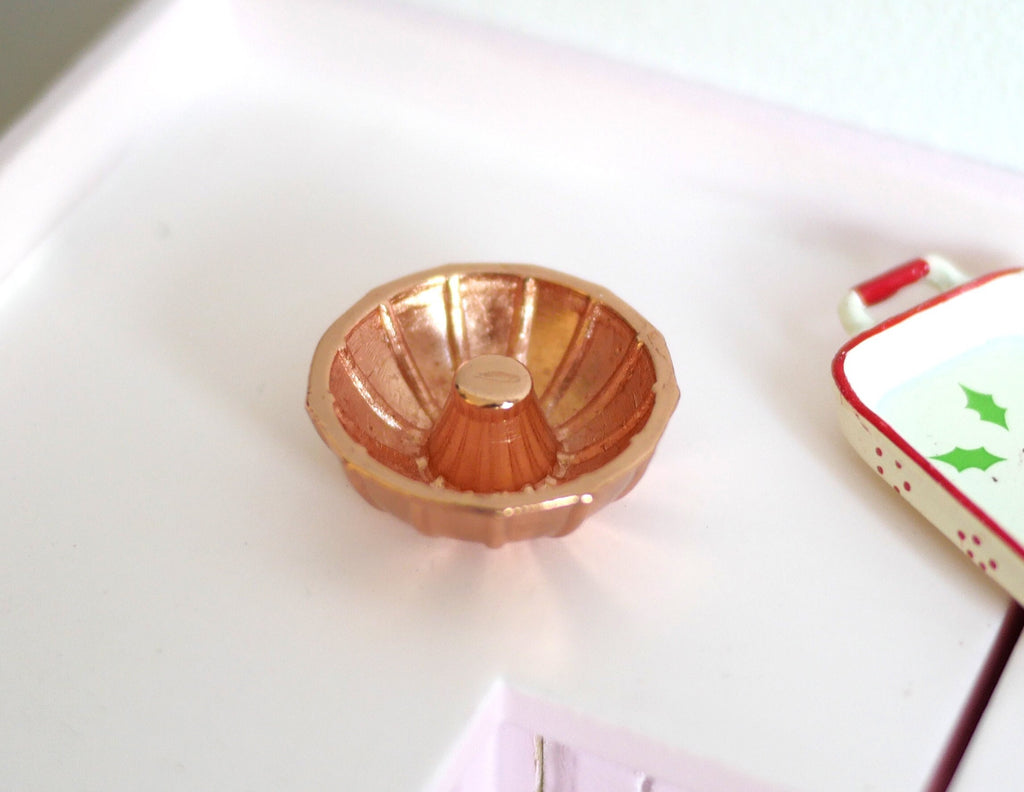 1:12 scale miniature metal bundt cake pan in copper with fluted sides and center tube, on a white kitchen counter