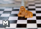1:12 scale miniature lying puppy dog figure in golden brown, shown on a black and white checkered floor