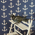 1:12 scale miniature black crow figure, perched on a white slatted shelf against anchor print wallpaper