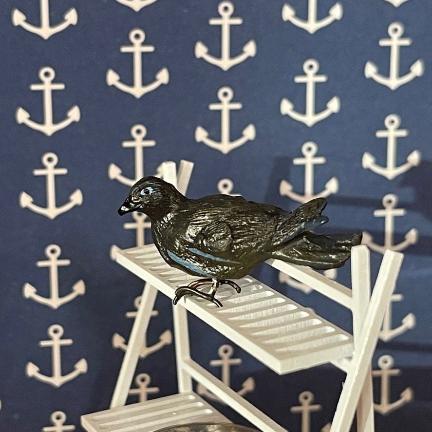 1:12 scale miniature black crow figure, perched on a white slatted shelf against anchor print wallpaper
