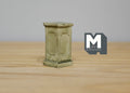 1:12 scale miniature square garden pedestal for plants in gray with paneled sides and a weathered finish, on a wood table
