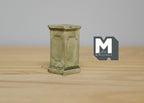 1:12 scale miniature square garden pedestal for plants in gray with paneled sides and a weathered finish, on a wood table