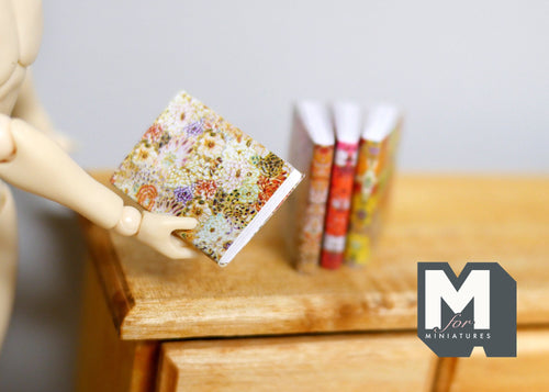 1:12 scale miniature books that open with floral covers, set of 4, shown on a wood dresser with a wooden artist figure