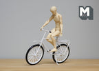 1:12 scale miniature metal leisure bicycle in white and black with spinning wheels, ridden by a wooden artist figure
