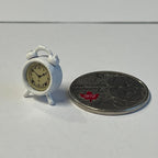 1:12 scale miniature metal twin bell alarm clock in white with a cream dial, shown beside a coin for scale