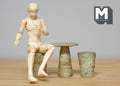 1:12 scale miniature stone look garden table and stools in gray, set of 3, shown with a seated artist figure