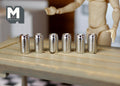 1:12 scale miniature silver drink cans with pull tabs, set of 6, lined up on a wood table beside an artist figure