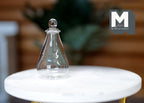 1:12 scale miniature clear glass conical flask with ball stopper, shown on a white marble side table
