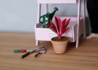 1:12 scale miniature potted red cordyline plant in clay pot, spiky red leaves, shown beside garden tools