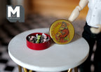 1:12 scale miniature red Christmas tin of chocolates with Santa print lid, shown open on a round white table
