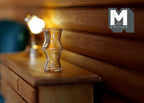 1:12 scale miniature glass vase with a curved hourglass shape, clear, shown on a wood dresser beside a lit lamp