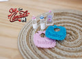 1:12 scale miniature baby feeding set of 5 with bottles, pink and blue bibs and baby oil, shown on a woven rug