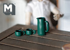 1:12 scale miniature water pot, kettle, cups and mug set in dark green, 5 pieces, shown on a dark wood table