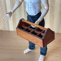 1:12 scale miniature wood garden tool caddy in dark brown with handle and divided slots, held by an artist figure