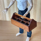 1:12 scale miniature wood garden tool caddy in dark brown with handle and divided slots, held by an artist figure