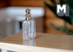 1:12 scale miniature clear glass jar with round stopper, square sided body, shown on a wood counter