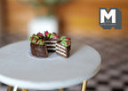 1:12 scale miniature chocolate cake with strawberries and kiwi, slice cut out showing layers, on a round white table