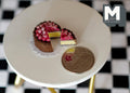 1:12 scale miniature chocolate cake with berries and a slice cut out, on its plate, on a white table beside a coin