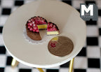 1:12 scale miniature chocolate cake with berries and a slice cut out, on its plate, on a white table beside a coin