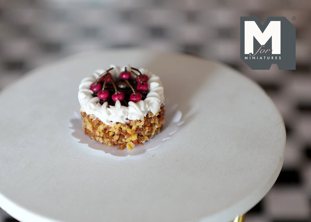 1:12 scale miniature cherry cake with cream and chopped nuts, topped with red cherries, on a round white table