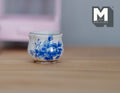 1:12 scale miniature ceramic flower pot in white with blue floral pattern, rounded shape, shown on a wood surface