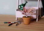 1:12 scale miniature potted pink variegated plant in clay pot, speckled pink leaves, shown beside garden tools