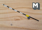 1:12 scale miniature fishing rod with reel in black and yellow with line and hook, shown on a wood surface