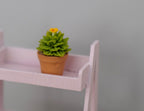 1:12 scale miniature potted round cactus with orange flower, short, green spiky rosette in a clay pot on a pink shelf