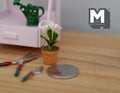 1:12 scale miniature potted flowers in white and pink in a terracotta pot, shown beside garden tools and a coin