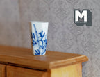 1:12 scale miniature ceramic tall cup vase in white with hand painted blue flowers, shown on a wood dresser
