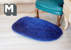 1:12 scale miniature small oval braided rug in royal blue, shown on a light wood floor beside a teal armchair