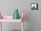 1:12 scale miniature ceramic bottle vase in teal green with a narrow neck, shown on a pink wood shelf