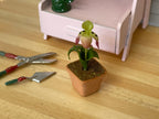 1:12 scale miniature potted yellow slipper orchid in square clay pot, single bloom with green leaves, beside garden tools
