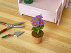 1:12 scale miniature potted flowers in purple and pink in a terracotta clay pot, shown beside garden tools