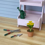 1:12 scale miniature potted yellow flowers in clay pot with green leaves, shown beside garden tools