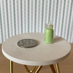 1:12 scale miniature real wax candle in glass jar in green with a wick, shown beside a coin on a round table