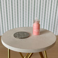 1:12 scale miniature pink wax candle in a glass jar with wick, shown on a round table beside a coin