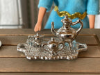 1:12 scale miniature silver tone English tea set with tray, set of 4, teapot, sugar and creamer, shown beside a doll